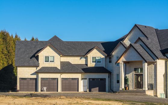 Giant brand new residential house with four stall garage and unpaved driveway in front