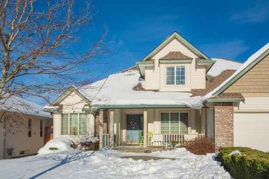 Entrance of luxury house with front yard in snow. Residential house on winter sunny day decorated for Christmas celebration