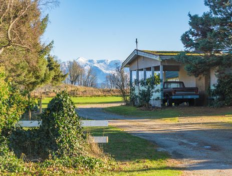 Back yard of family house with old truck parked under carport and mountain view background