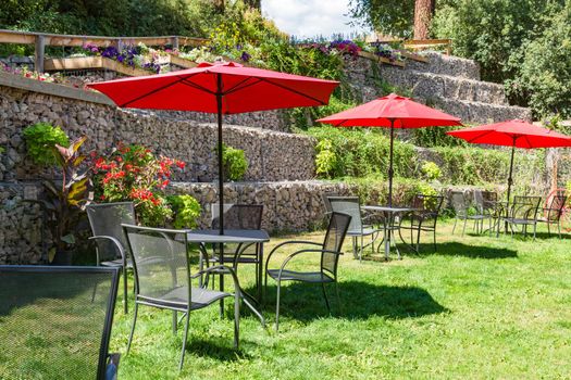Outside cafe tables on green lawn under the red umbrella canopies
