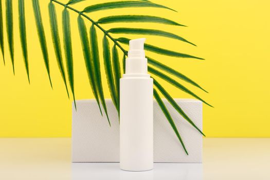 Summer face cream with SPF with white geometric podium with palm leaf against yellow background. Concept of sunscreen and skin care during summer