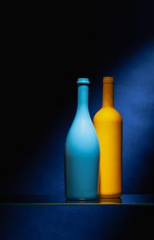 Two empty wine bottles on the glass table in the dark bar.Blue and yellow empty wine bottles.