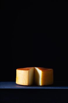Big round of hard cheese on the slate desk in the dark background.