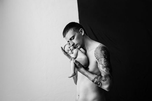 Father with tattoo on his arm is holding his newborn baby on a black and white background. High quality photo