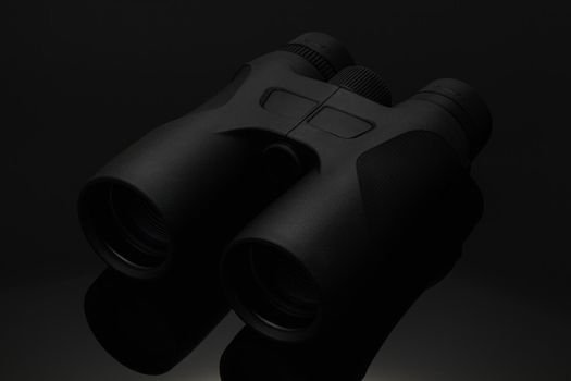 Black binocular isolated on black background. Hi tech black binocular on the black glass table. Studio shot.