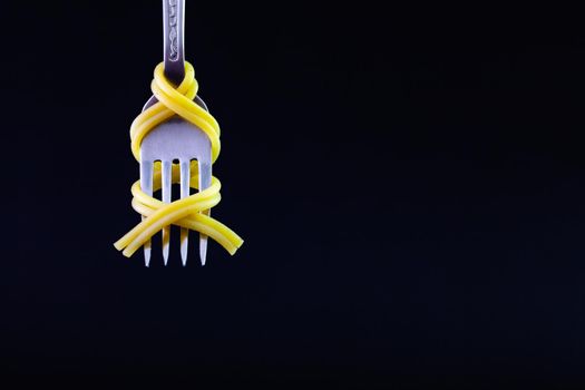 Freshly cooked pasta on a old fork on the black background. Symmetrical loop of spaghetti on an old fork.