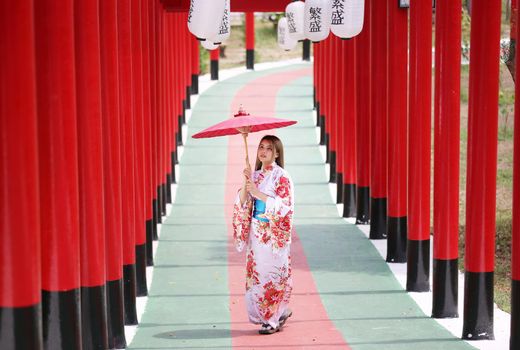 woman in kimono holding umbrella walking into at the shrine red gate, in Japanese garden.
