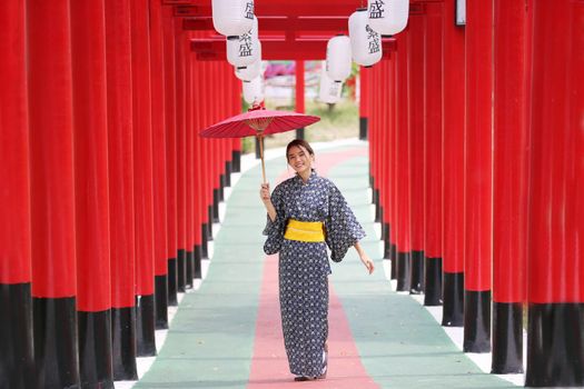 woman in kimono holding umbrella walking into at the shrine red gate, in Japanese garden.