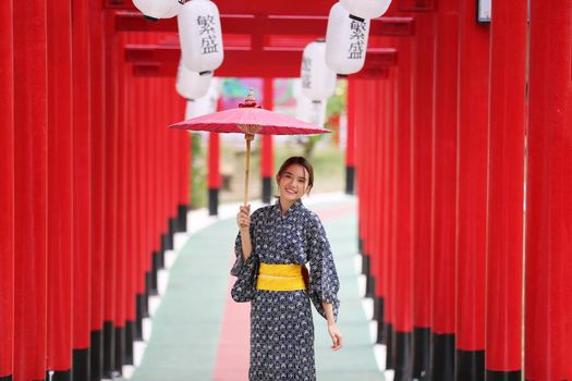 woman in kimono holding umbrella walking into at the shrine red gate, in Japanese garden.