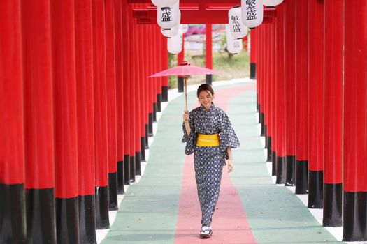 woman in kimono holding umbrella walking into at the shrine red gate, in Japanese garden.