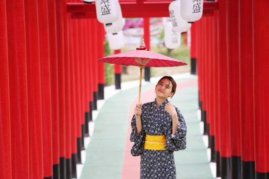 woman in kimono holding umbrella walking into at the shrine red gate, in Japanese garden.