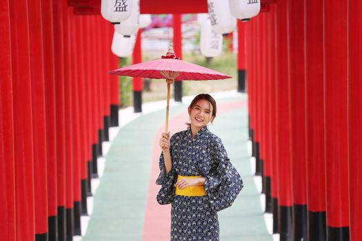 woman in kimono holding umbrella walking into at the shrine red gate, in Japanese garden.