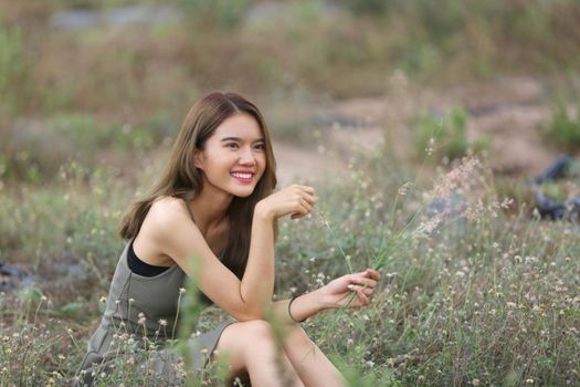 A beautiful woman with long hair in a dress sitting on a meadow and flowers in the evening light.