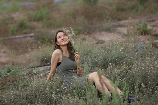 A beautiful woman with long hair in a dress sitting on a meadow and flowers in the evening light.