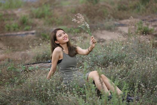 A beautiful woman with long hair in a dress sitting on a meadow and flowers in the evening light.