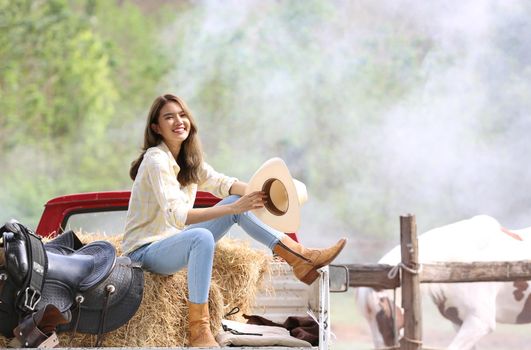 A woman in a cowgirl style sits in a horse ranch with a western farm environment.