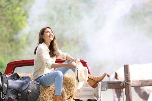 A woman in a cowgirl style sits in a horse ranch with a western farm environment.
