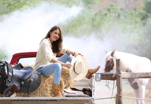 A woman in a cowgirl style sits in a horse ranch with a western farm environment.