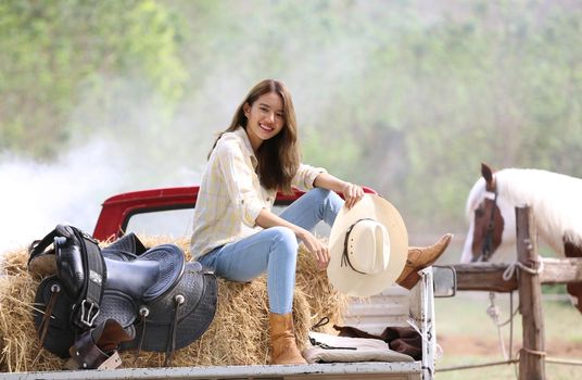 A woman in a cowgirl style sits in a horse ranch with a western farm environment.