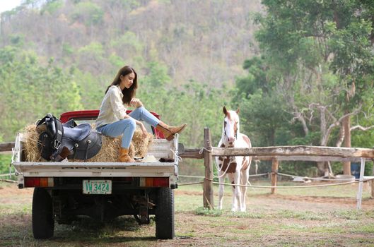 A woman in a cowgirl style sits in a horse ranch with a western farm environment.