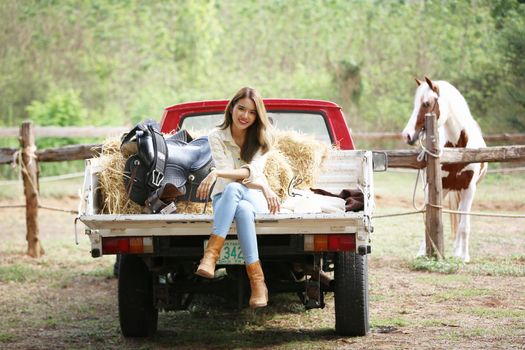 A woman in a cowgirl style sits in a horse ranch with a western farm environment.