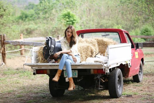 A woman in a cowgirl style sits in a horse ranch with a western farm environment.