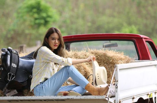 A woman in a cowgirl style sits in a horse ranch with a western farm environment.