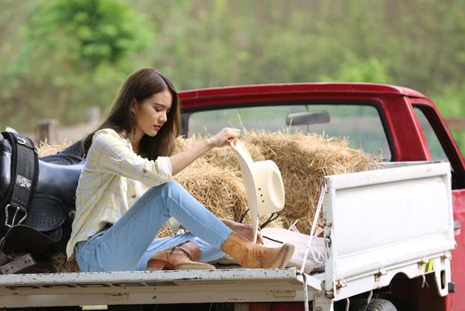 A woman in a cowgirl style sits in a horse ranch with a western farm environment.
