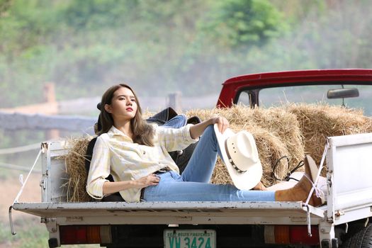 A woman in a cowgirl style sits in a horse ranch with a western farm environment.