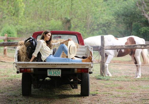 A woman in a cowgirl style sits in a horse ranch with a western farm environment.