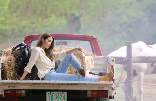 A woman in a cowgirl style sits in a horse ranch with a western farm environment.