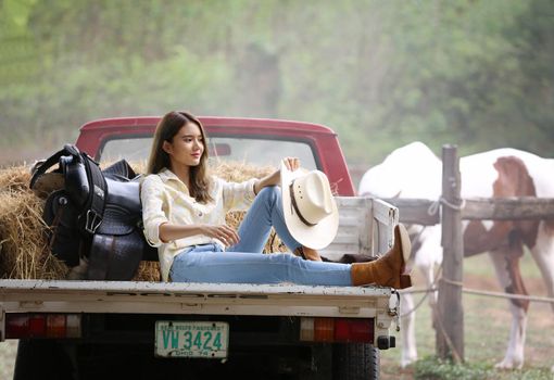 A woman in a cowgirl style sits in a horse ranch with a western farm environment.