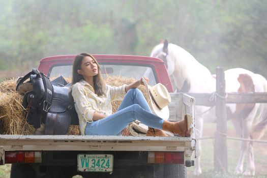 A woman in a cowgirl style sits in a horse ranch with a western farm environment.