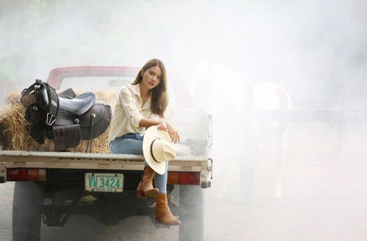 A woman in a cowgirl style sits in a horse ranch with a western farm environment.