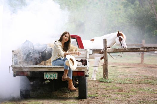 A woman in a cowgirl style sits in a horse ranch with a western farm environment.