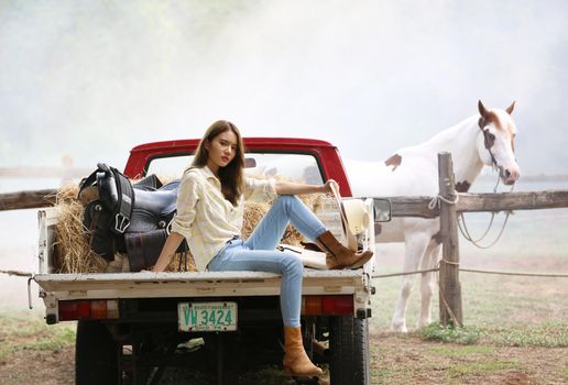 A woman in a cowgirl style sits in a horse ranch with a western farm environment.