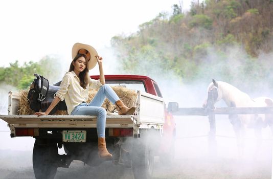 A woman in a cowgirl style sits in a horse ranch with a western farm environment.