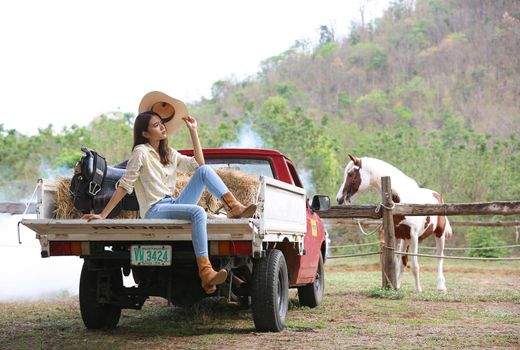 A woman in a cowgirl style sits in a horse ranch with a western farm environment.