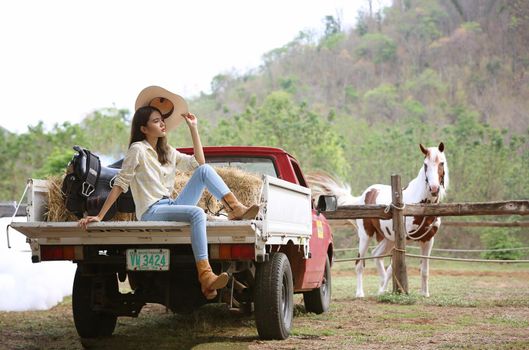 A woman in a cowgirl style sits in a horse ranch with a western farm environment.