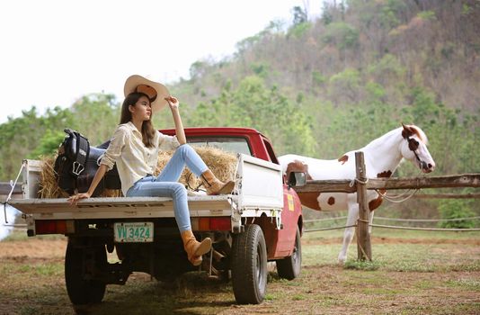 A woman in a cowgirl style sits in a horse ranch with a western farm environment.
