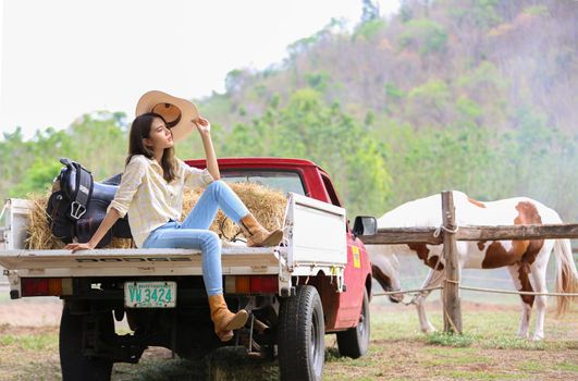 A woman in a cowgirl style sits in a horse ranch with a western farm environment.