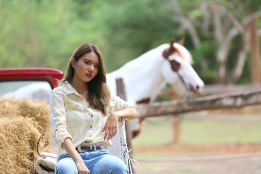 A woman in a cowgirl style sits in a horse ranch with a western farm environment.