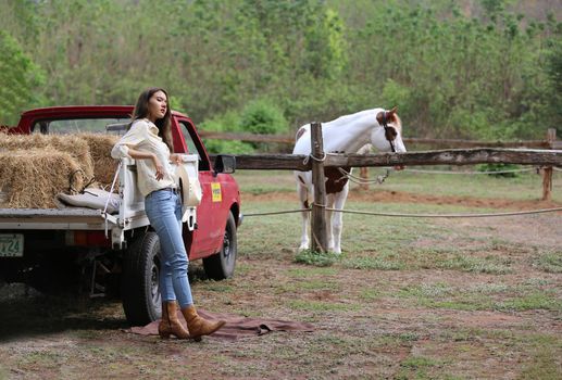 A woman in a cowgirl style sits in a horse ranch with a western farm environment.