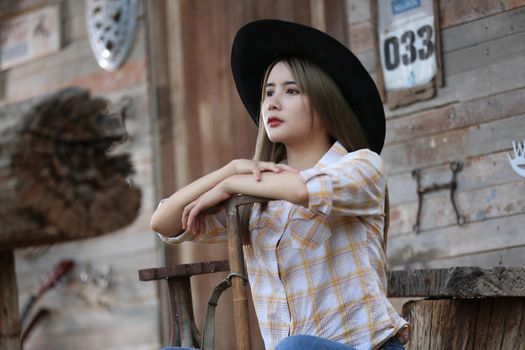 A woman in a cowgirl style sits in a horse ranch with a western farm environment.