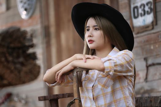 A woman in a cowgirl style sits in a horse ranch with a western farm environment.
