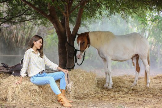 A woman in a cowgirl style sits in a horse ranch with a western farm environment.