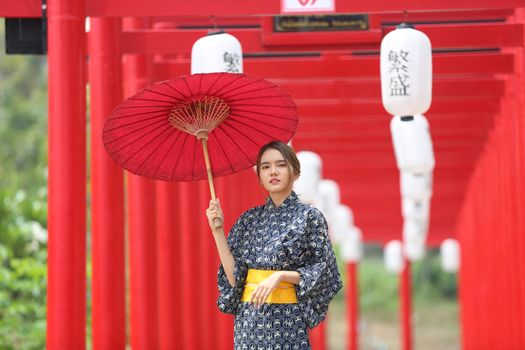 woman in kimono holding umbrella walking into at the shrine red gate, in Japanese garden.