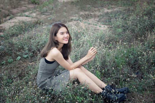 A beautiful woman with long hair in a dress sitting on a meadow and flowers in the evening light.