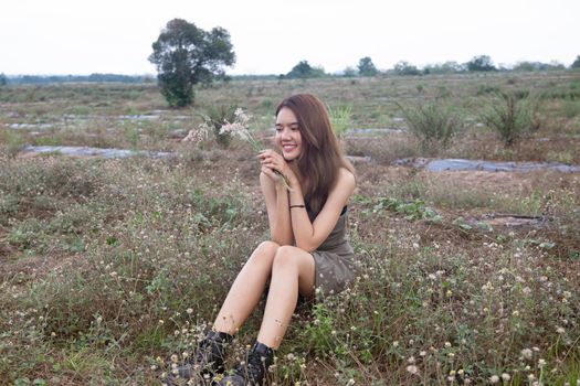 A beautiful woman with long hair in a dress sitting on a meadow and flowers in the evening light.