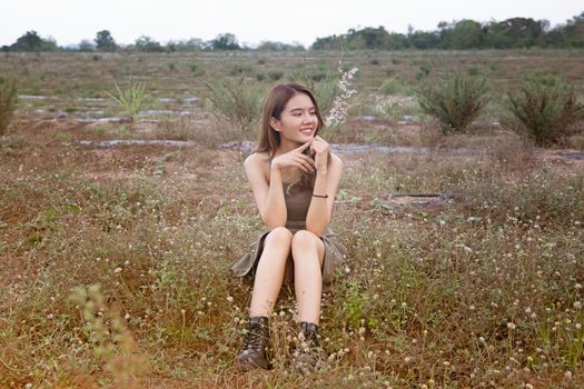 A beautiful woman with long hair in a dress sitting on a meadow and flowers in the evening light.
